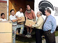 Chaplain George Holley hands a box to Manna Food Bank worker. Superintendent William Anderson looks on.